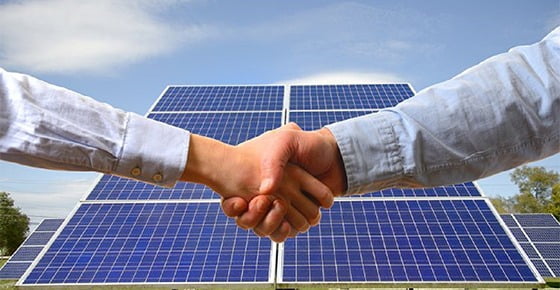 hand shaking with commercial solar panels in the background