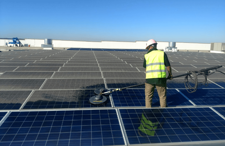 a solar expert cleaning solar panels with long handled soft brush