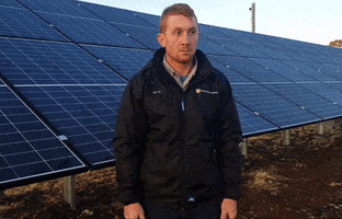 man expressing a sense of doubt standing beside solar panels